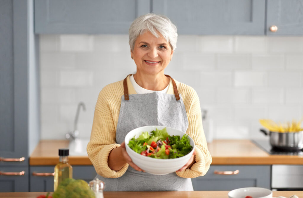 An elderly woman holding a bowl with healthy salad in her hand.