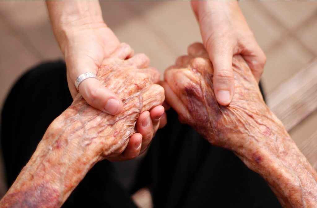 Daughter holding both of senior mothers hand while sitting down