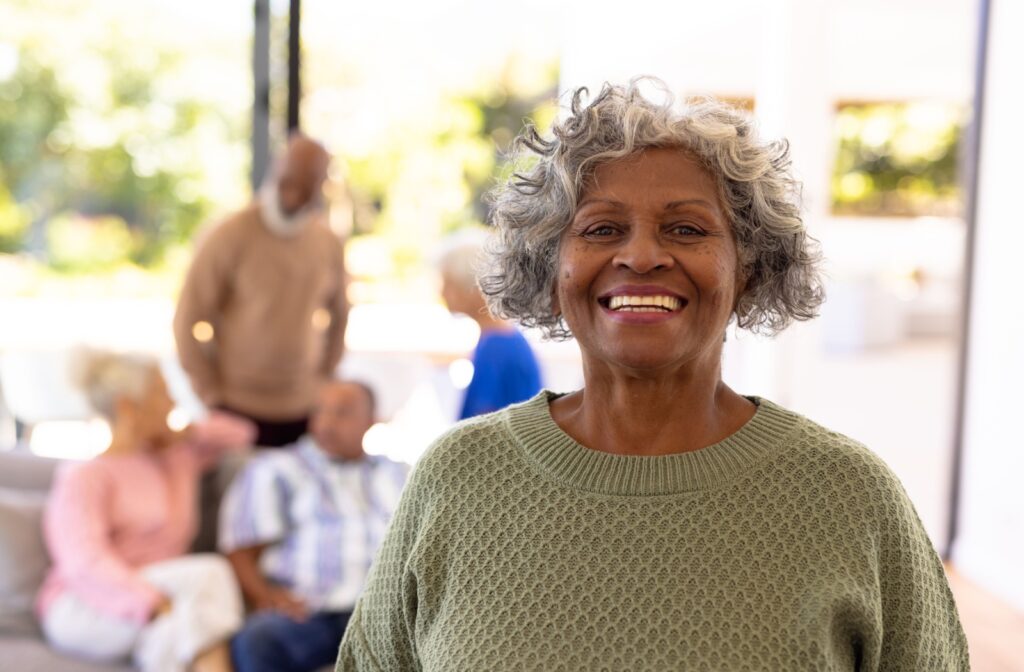 A senior woman smiling while at her new assisted living community with other seniors chatting in the background