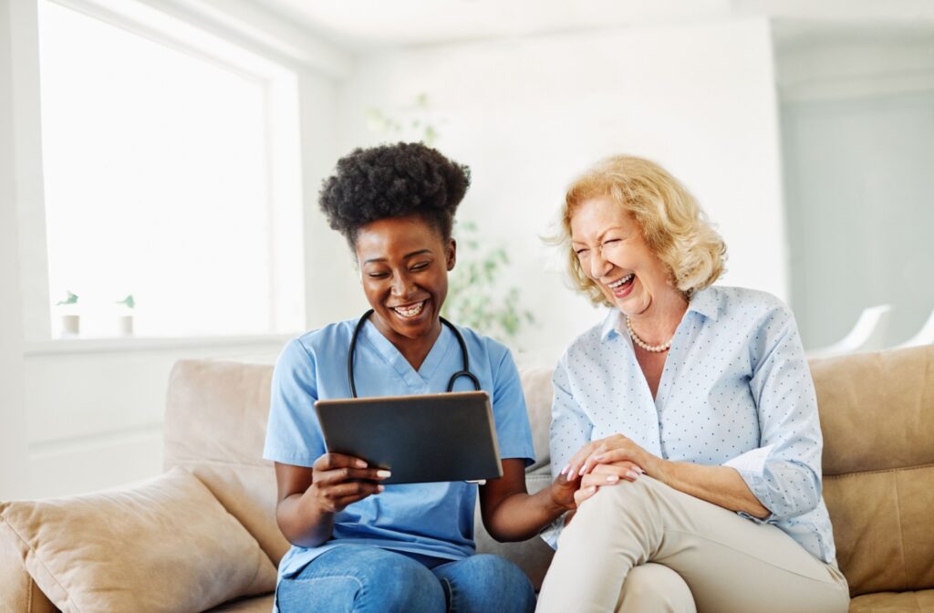 A skilled caregiver and senior sit together, laughing, and reviewing the senior's health plan.