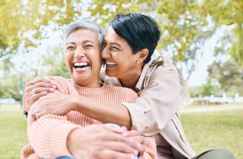 A laughing senior couple embrace while sitting on a lawn outside of their assisted living community, enjoying life