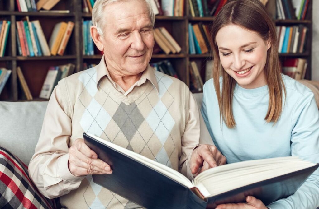 A young adult visiting their grandparent in memory care goes through a photo album together during a visit