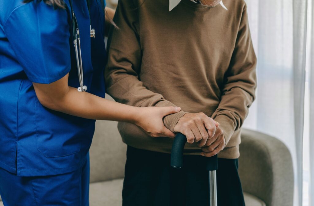 A nurse holds the arm of a senior holding a cane, providing additional movement support in an assisted living community.
